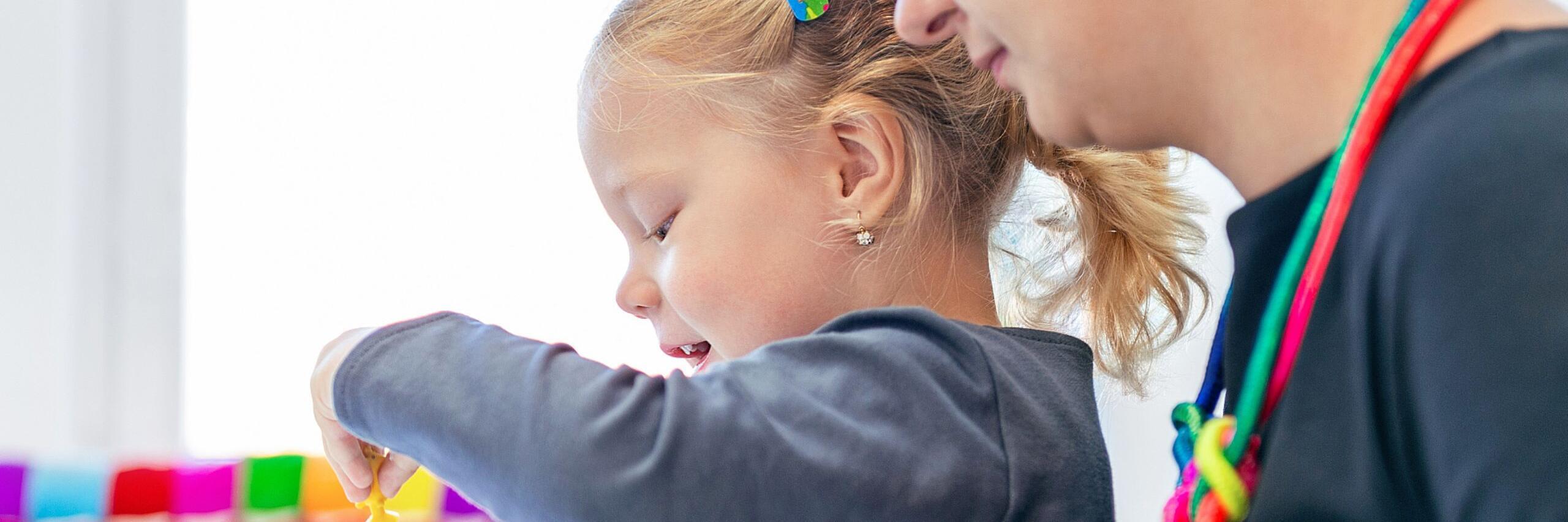 Johanniter-Erzieherin begleitet ein spielendes Mädchen beim Basteln mit bunten Figuren.