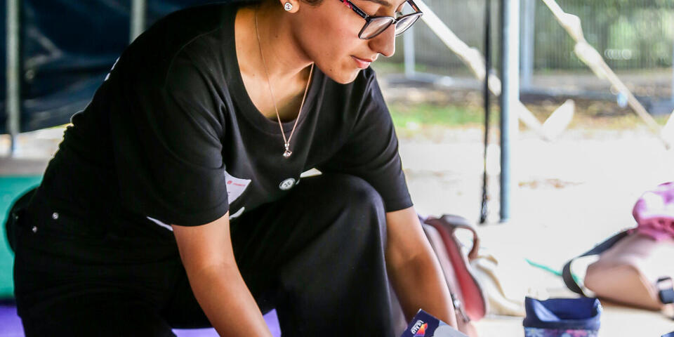 Betreuerin kniet im Zelt und sortiert Mitmachhefte; daneben Taschen und Gummistiefel.