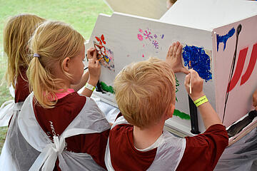 Kinder bemalen gemeinsam eine große weiße Fläche bei einer Kreativaufgabe.