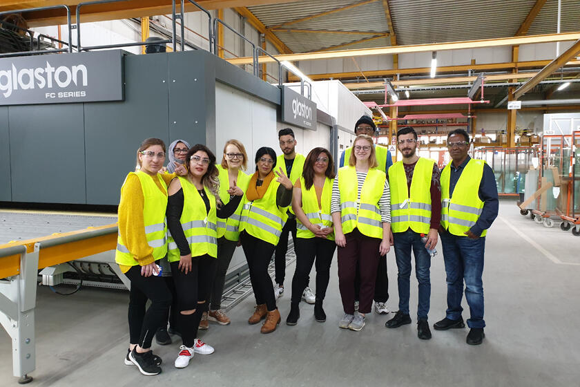 Teilnehmende der Erstorientierungskurse und ihre Lehrkräfte stehen in der Produktionshalle der Interpane Glasindustrie AG. 