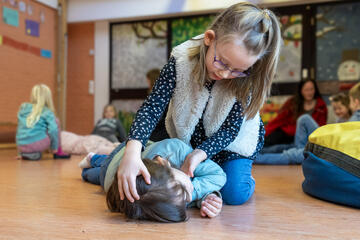 Ein Mädchen führt an einem anderen die stabile Seitenlage durch. Gerade überstreckt sie vorsichtig den Kopf.