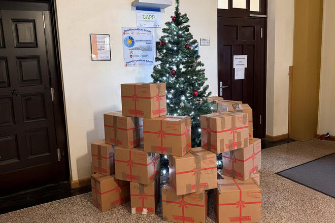  In einer Schulhalle stehen Weihnachtstrucker-Pakete vor einem Weihnachtsbaum