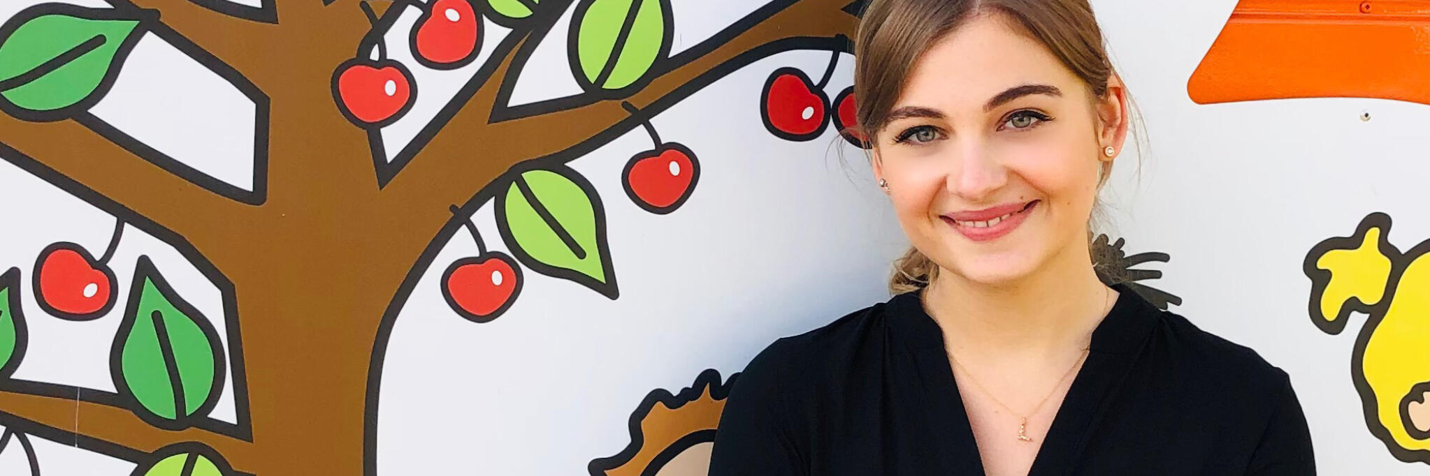 Linda, Leitung der Johanniter-Kita Kirschbaum vor einer Kirschbaum-Wand.