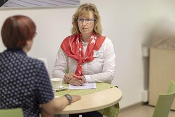 Leiterin Bettina Wichmann sitzt am Tisch und spricht mit einer Dame. 