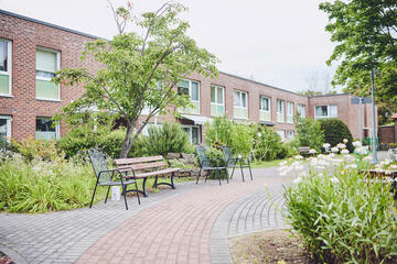 Gartenbänke stehen in der gepflegten Anlage des Johanniter-Stift Gut Heuserhof in Köln.