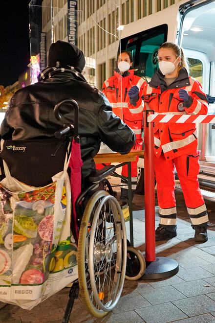 Zwei Helfende des Kältebus geben Lebensmittel an einen Mann im Rollstuhl