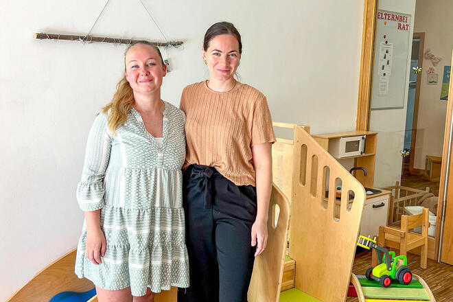 Zwei Frauen stehen vor einer Kinderrutsche und lächeln in die Kamera.