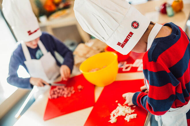Zwei Kinder mit Johanniter Kochschürzen- und Mützen schneiden Gemüse
