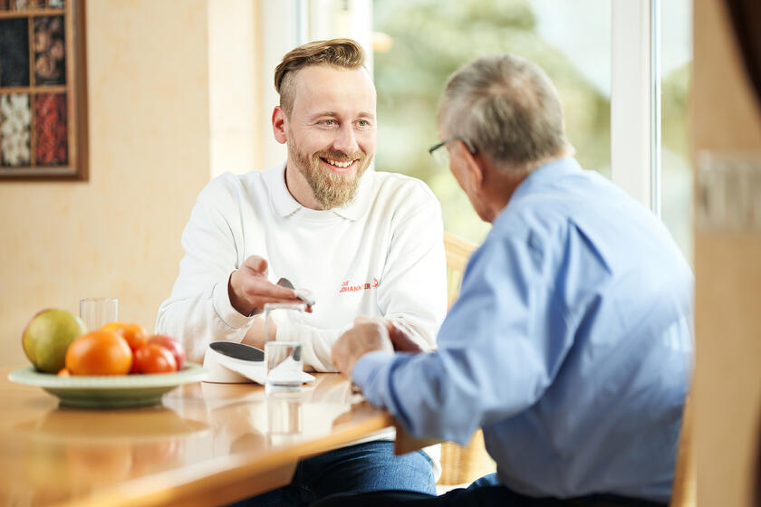 Ein Mitarbeiter der Johanniter-Unfall-Hilfe im Gespräch mit einem Hausnotruf-Kunden.