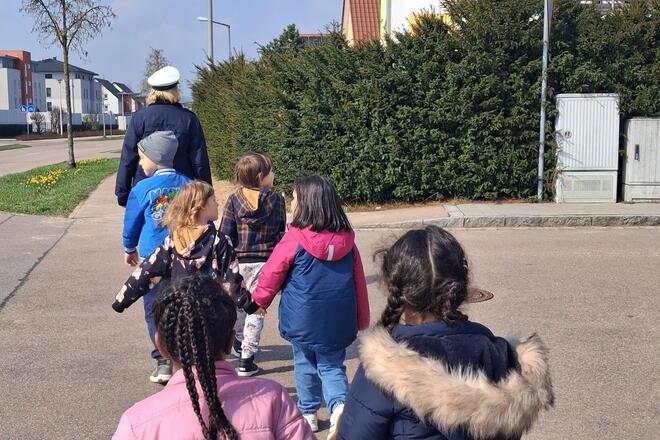 Vorschulkinder überqueren gemeinsam mit Polizistin die Straße.