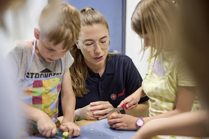 Kinderküche: Johanniter Betreuungskraft erklärt, wie man Gemüse richtig schneidet.