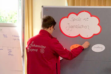 Ein junger Erwachsener steht vor einer Pinnwand und ergänzt zum Thema "Spiele mit Jugendlichen"