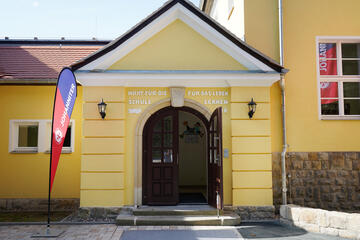 ein gelbes Haus mit Fahnen der Johanniter davor 