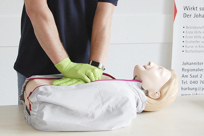 Ein Erste-Hilfe-Ausbilder mit Maske führt eine Herzmassage an einer Puppe vor