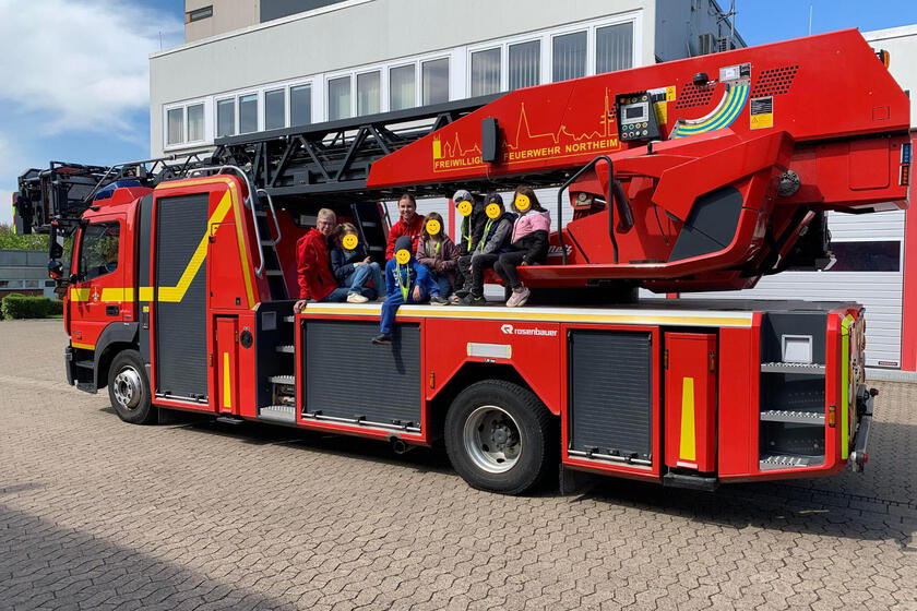 Kinder und zwei Erzieherinnen sitzen auf einem Feuerwehrfahrzeug