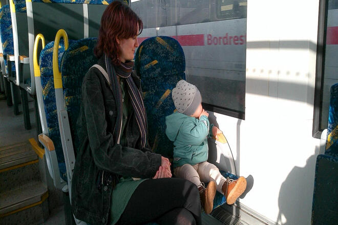 Eine Frau mit einem Kleinkind im Zug. Das Kind schaut aus dem Fenster und sieht einen weiteren Zug