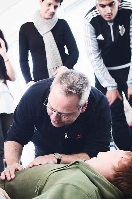 Ein Mann übt an einer Person die Wiederbelebung, während andere zuschauen.