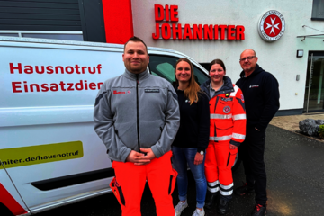 Vier Mitarbeitende aus dem Johanniter-Hausnotruf stehen aufgereiht vor einem Johanniter-Fahrzeug - das wiederum vor der Johanniter-Regionalgeschäftsstelle steht. Das Gebäude trägt das Johanniter-Logo über dem Eingang.