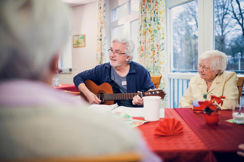 Ein Mitarbeiter spielt Gitarre und eine Gruppe von Bewohnenden hört zu