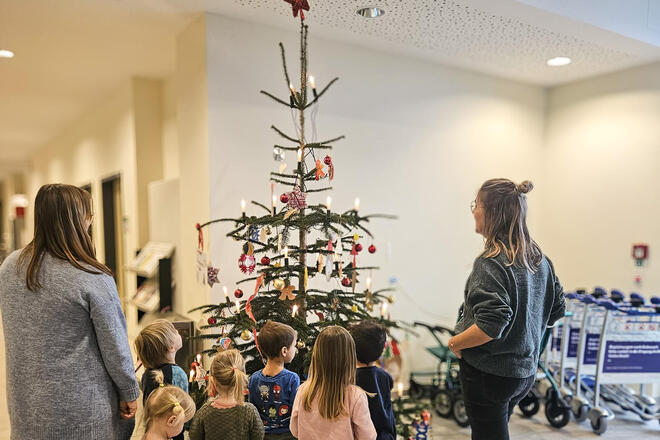 Kinder und zwei Frauen vor einem geschmückten Weihnachtsbaum in einem Krankenhaus