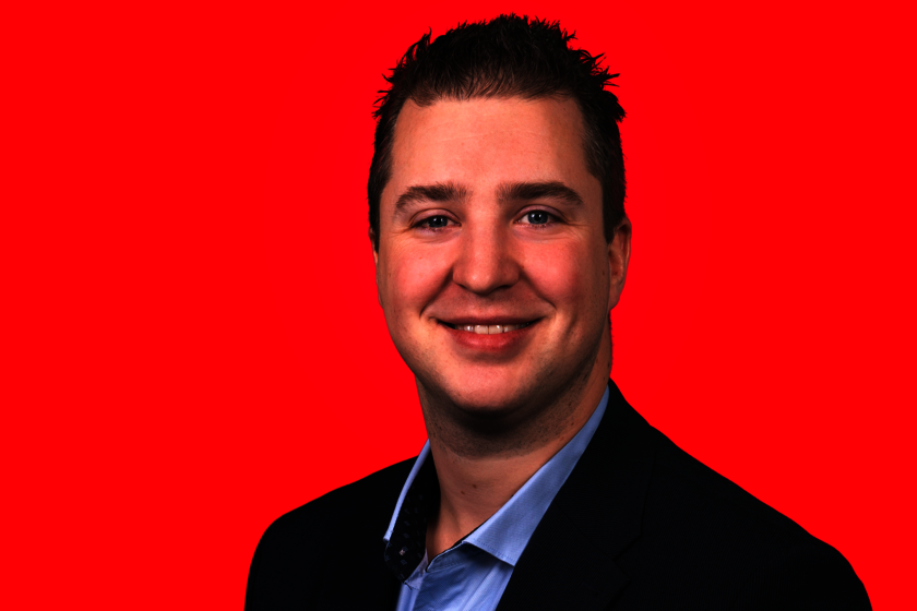 Ein Porträitfoto von einer männlichen Person vor rotem Hintergrund