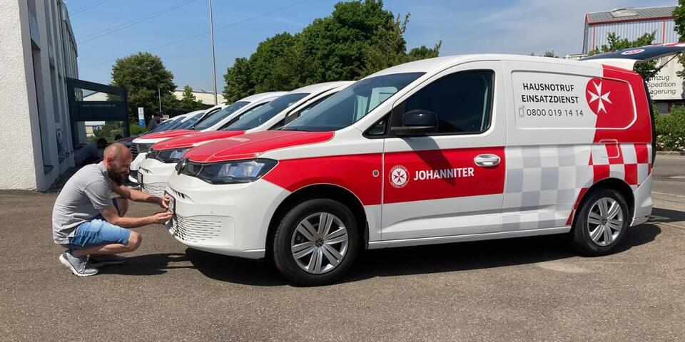 Ein Johanniter bringt das KfZ-Kennzeichen an seinem neuen Fahrzeug an