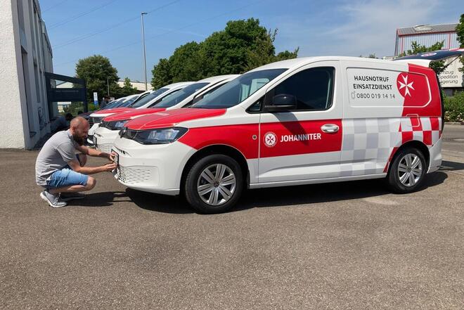 Ein Johanniter bringt das KfZ-Kennzeichen an seinem neuen Fahrzeug an