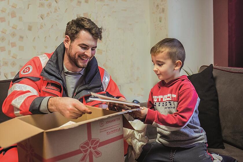 Ein Mitarbeiter der Johanniter packt mit einem kleinen Jungen ein Weihnachtspaket aus