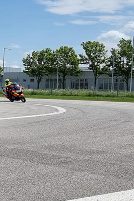 Zwei Einsatzkräfte der Johanniter-Motorradstaffel üben mit ihren Einsatzmotorrädern auf einem Trainingsplatz bei sonnigem Wetter. Sie tragen gelbe Helme und reflektierende Kleidung.