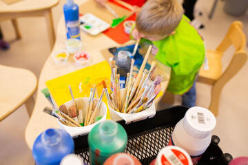 Kinder malen im Kreativraum, Farben und Pinsel stehen nebendran