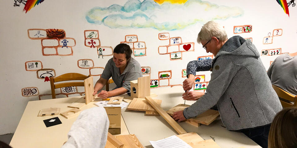 Zwei Frauen basteln in einem Gemeinschaftsraum an Vogelhäusern.