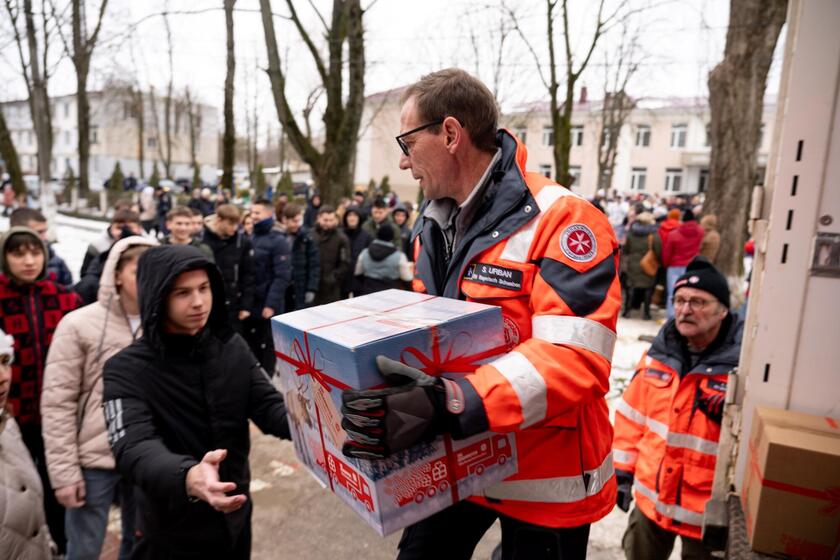 Ein Johanniter gibt einer jungen Person ein Paket vom Weihnachtstrucker.