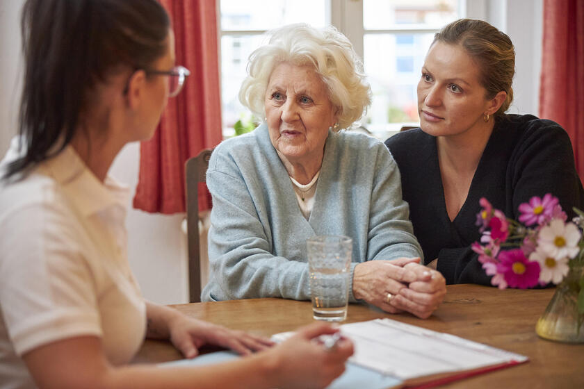 Eine Johanniterin berät eine ältere Frau, die neben einer weiteren Frau sitzt.