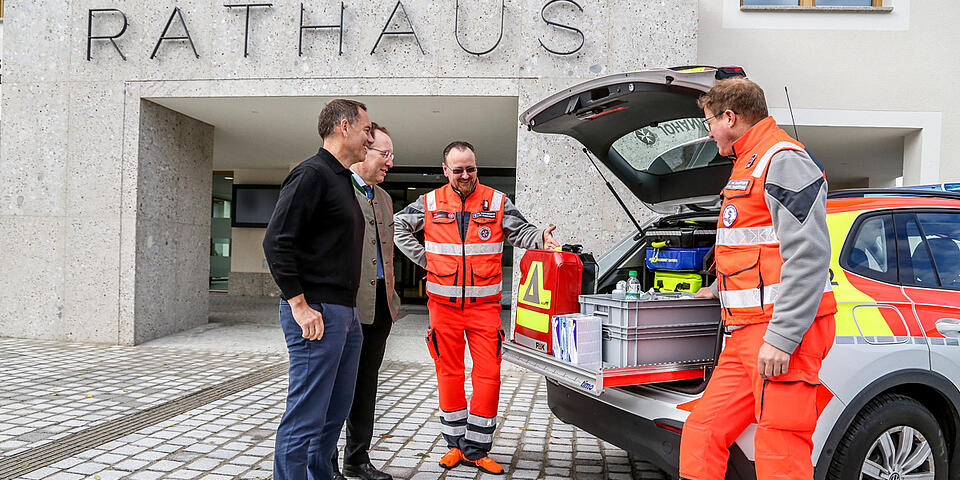 Zwei Bürgermeister stehen vor der geöffneten Heckklappe ds EinsatzFahrzeugs und erhalten von Einsatzkräften Erklärungen zur Ausstattung.