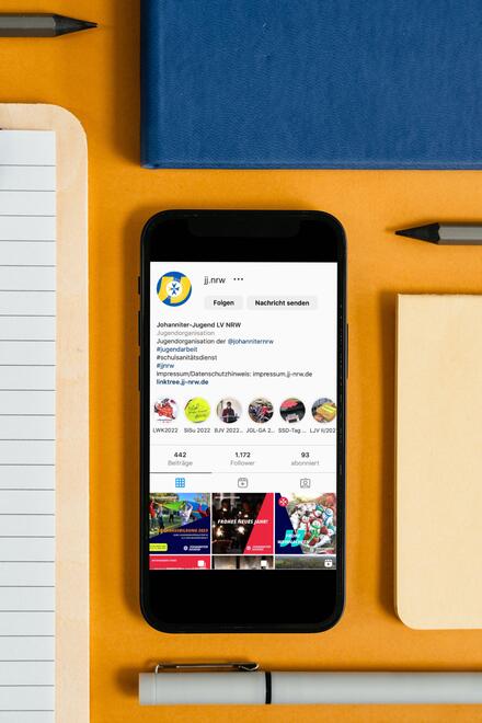Ein Handy liegt auf einem Tisch. Darauf ist die Instagram-Seite der Johanniter-Jugend NRW geöffnet.