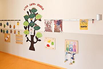 Eine Wand in einer Kita, dekoriert mit einem großen Papierbaum und mehreren Kinderzeichnungen, die an einer Leine befestigt sind.