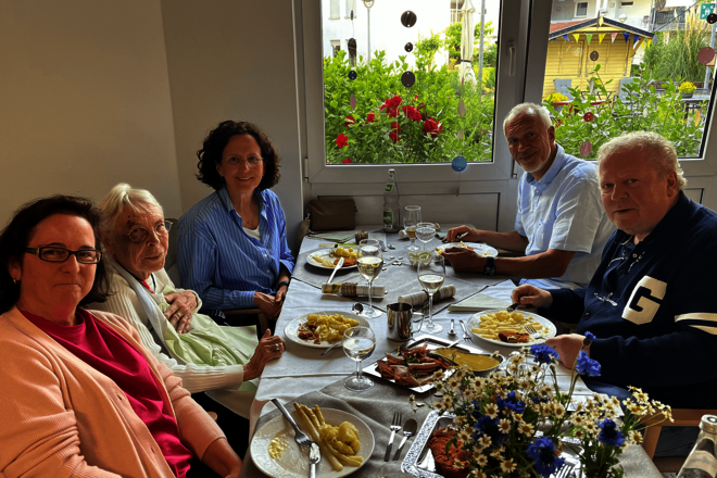 Fünf Personen unterschiedlichen Alters sitzen vor gefüllten Tellern an einem geschmückten Tisch