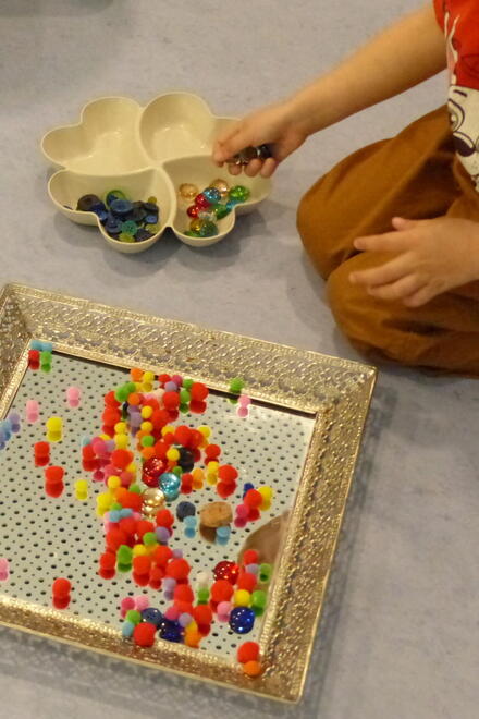 Ein Kind auf dem Boden spielt mit bunten Kugeln und Murmeln und legt sie auf einen Spiegel.
