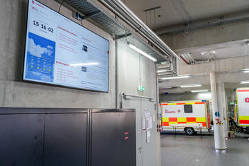 Fahrzeughalle mit zwei geparkten Rettungswagen, Monitor mit Informationen im Vordergrund.