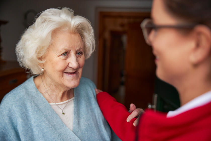 Seniorin lächelt, jüngere Frau legt beruhigend die Hand auf ihre Schulter.