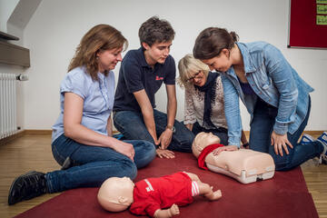 Jugendliche üben unter Anleitung die Herz‑Lungen‑Wiederbelebung an Kinder-Übungspuppen.