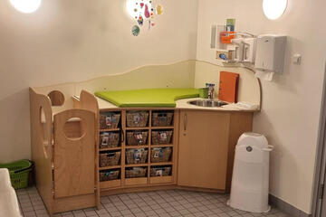 Wickeltisch mit grüner Matte und untern vielen Körbchen mit Wechselsachen für die Kinder.