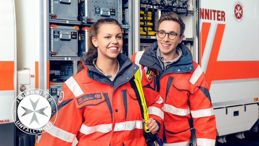 Zwi Ehrenamtliche der Johanniter stehen vor einem Einsatzwagen