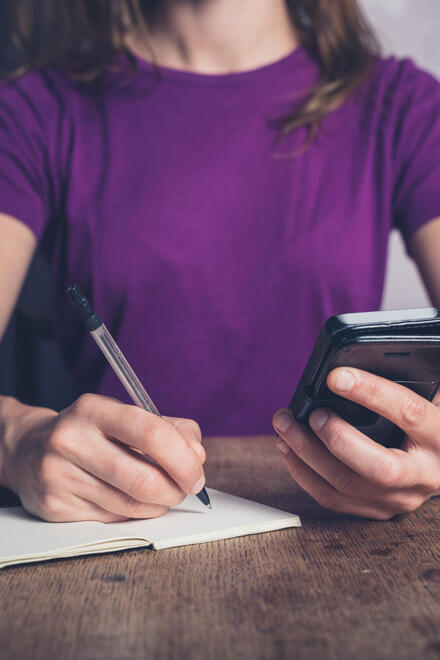 Eine Frau schreibt Daten aus ihrem Handy auf ein Blatt Papier.