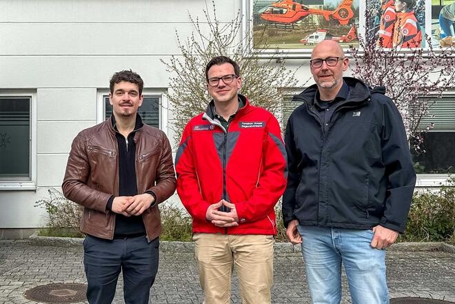 Drei Männer stehen vor der Geschäftsstelle der Johanniter in Lübeck und lächeln in die Kamera.