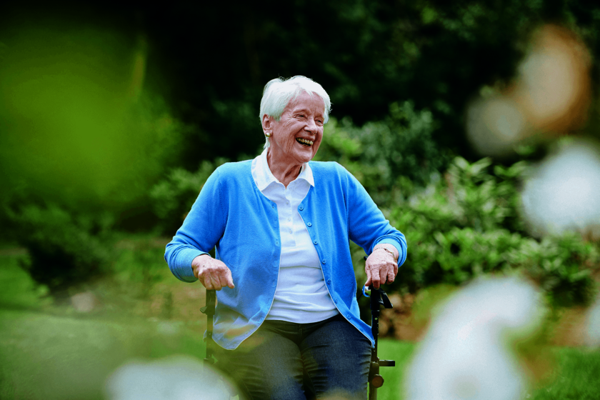 Ältere Frau lacht im Rollstuhl im Grünen.