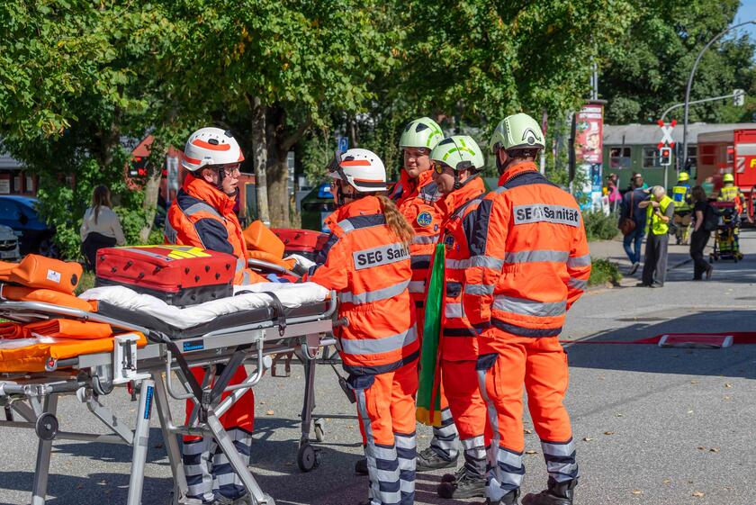 Fünf Ehrenamtliche in Einsatzkleidung stehen an einer Trage und warten auf ihren Einsatz.