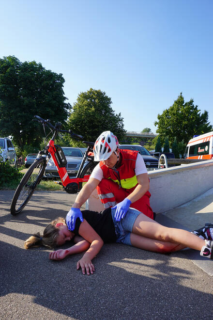 Frau liegt verletzt auf dem Boden. Sanitäter der Fahrradstaffel kontrolliert die Vitalwerte.
