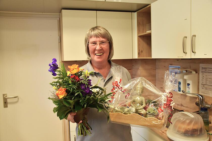 eine Mitarbeiterin hält ihr Abschiedsgeschenk und einen Blumenstrauß in Händen