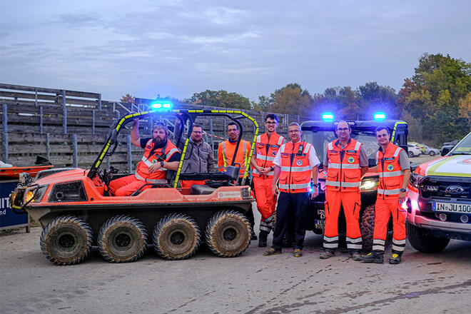 7 Männer in Einsatzkleidung stehen in Mitten von verschiedenen Einsatzfahrzeugen.